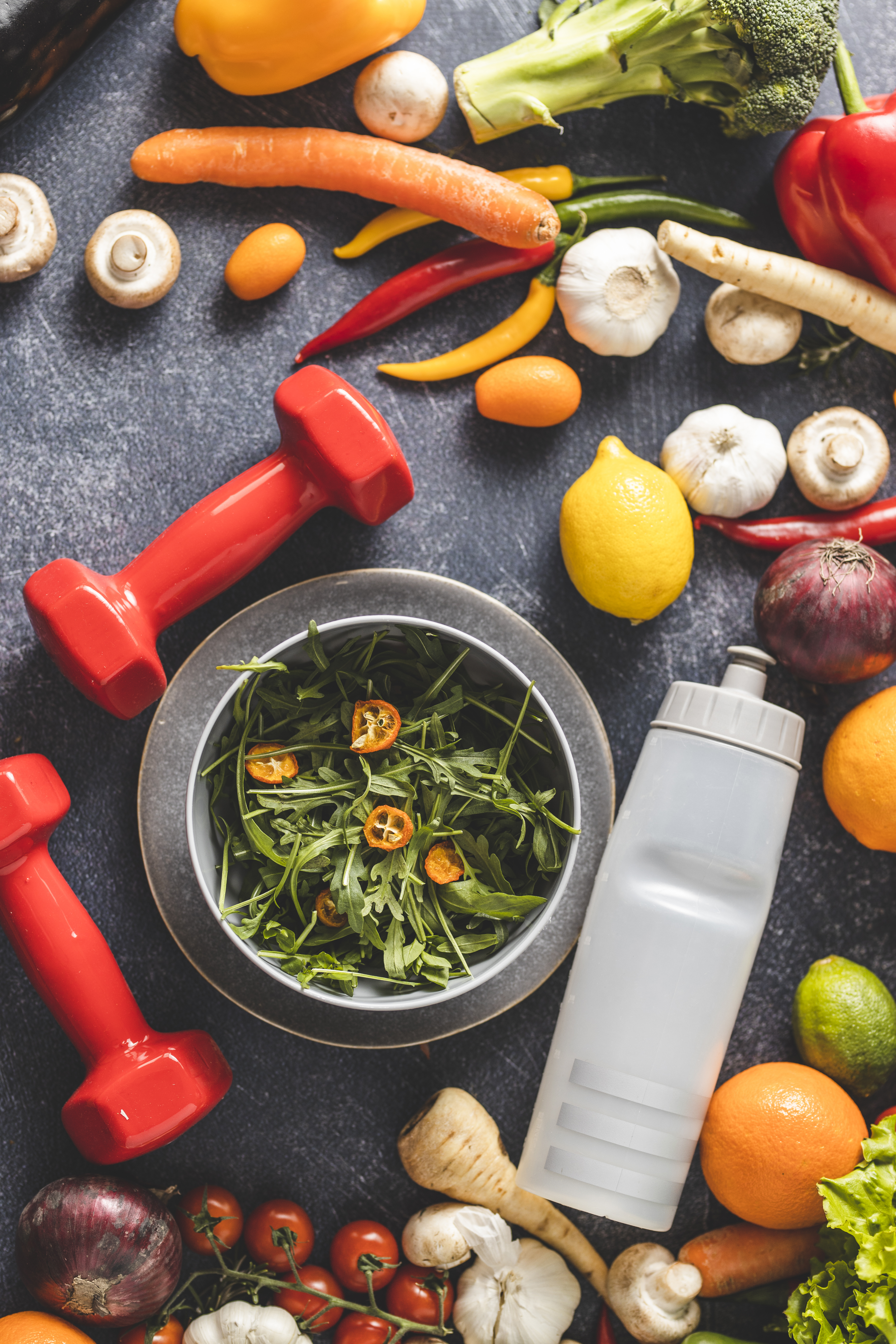 Female dumbbells, vegetables, fruit and sport's bottle isolated on dark background