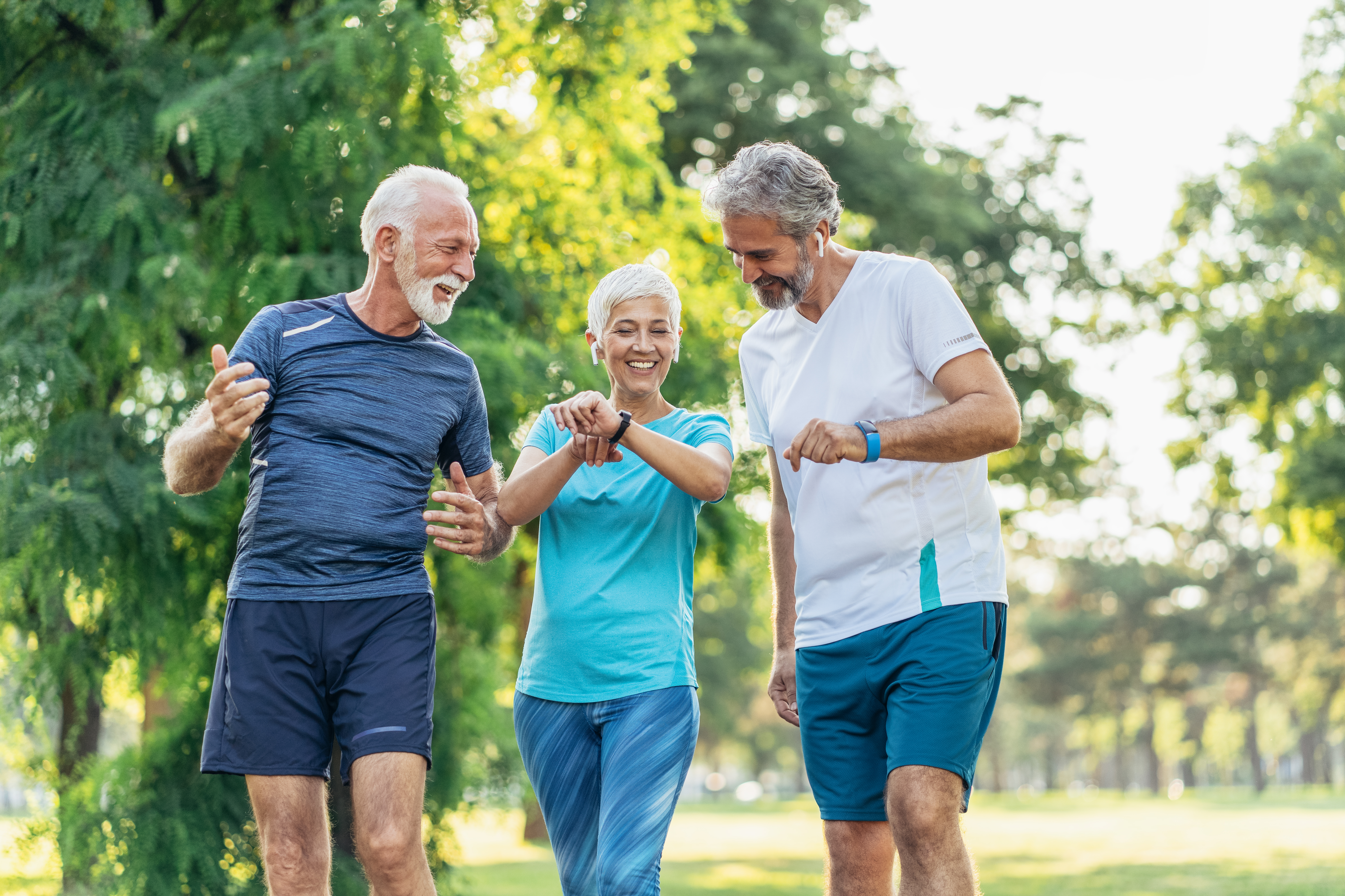 Three senior athletes in the park using digital devices after jogging