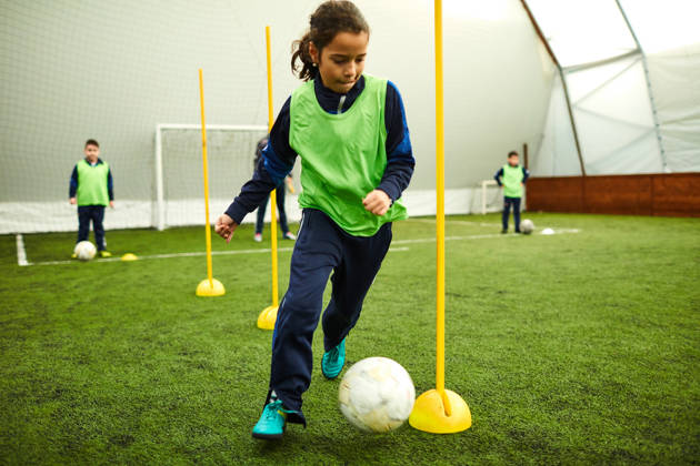 Meisje dribbelt met bal tussen kegels