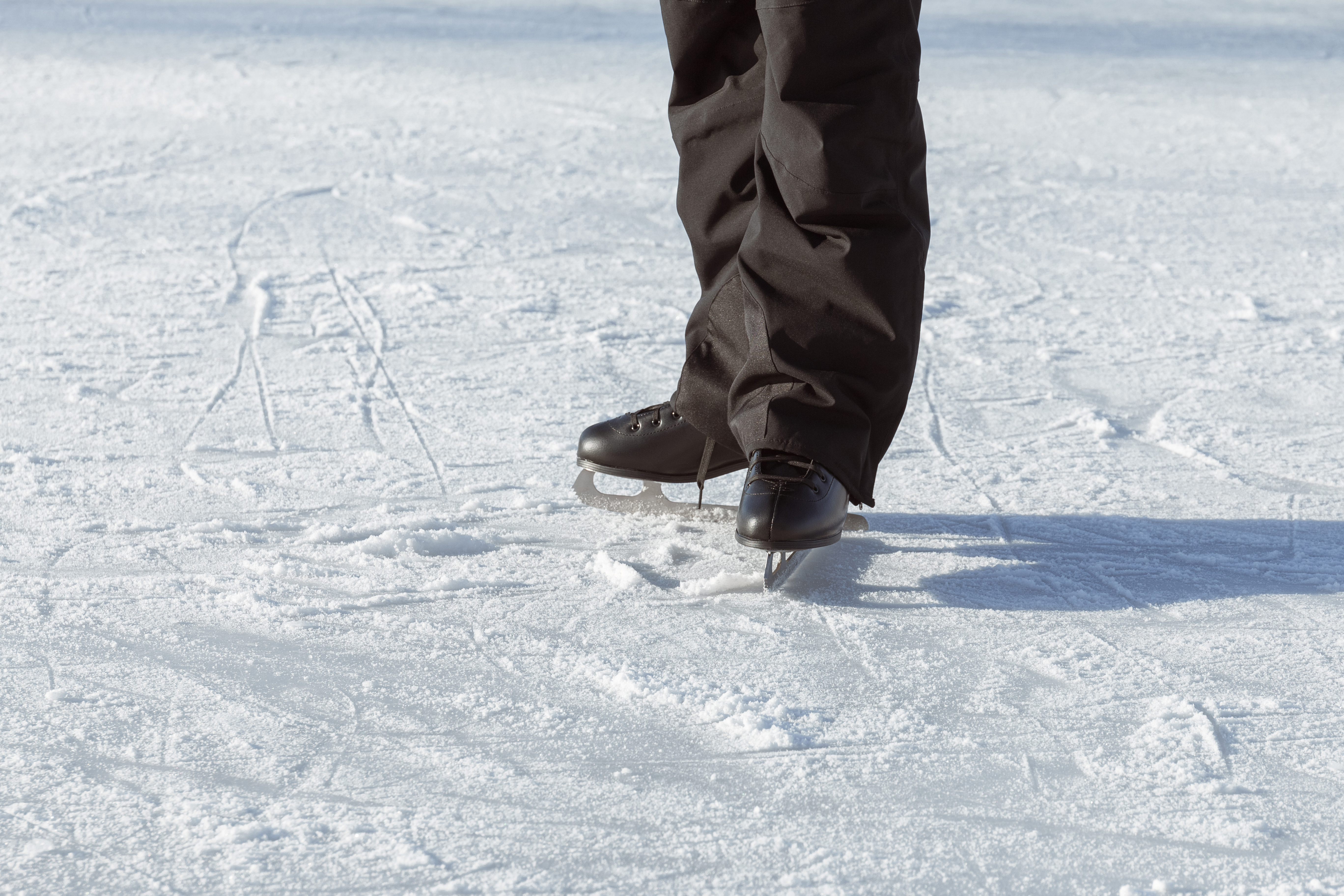 Men's legs in black skates close-up, standing on the rink facing the sun. Active winter holidays