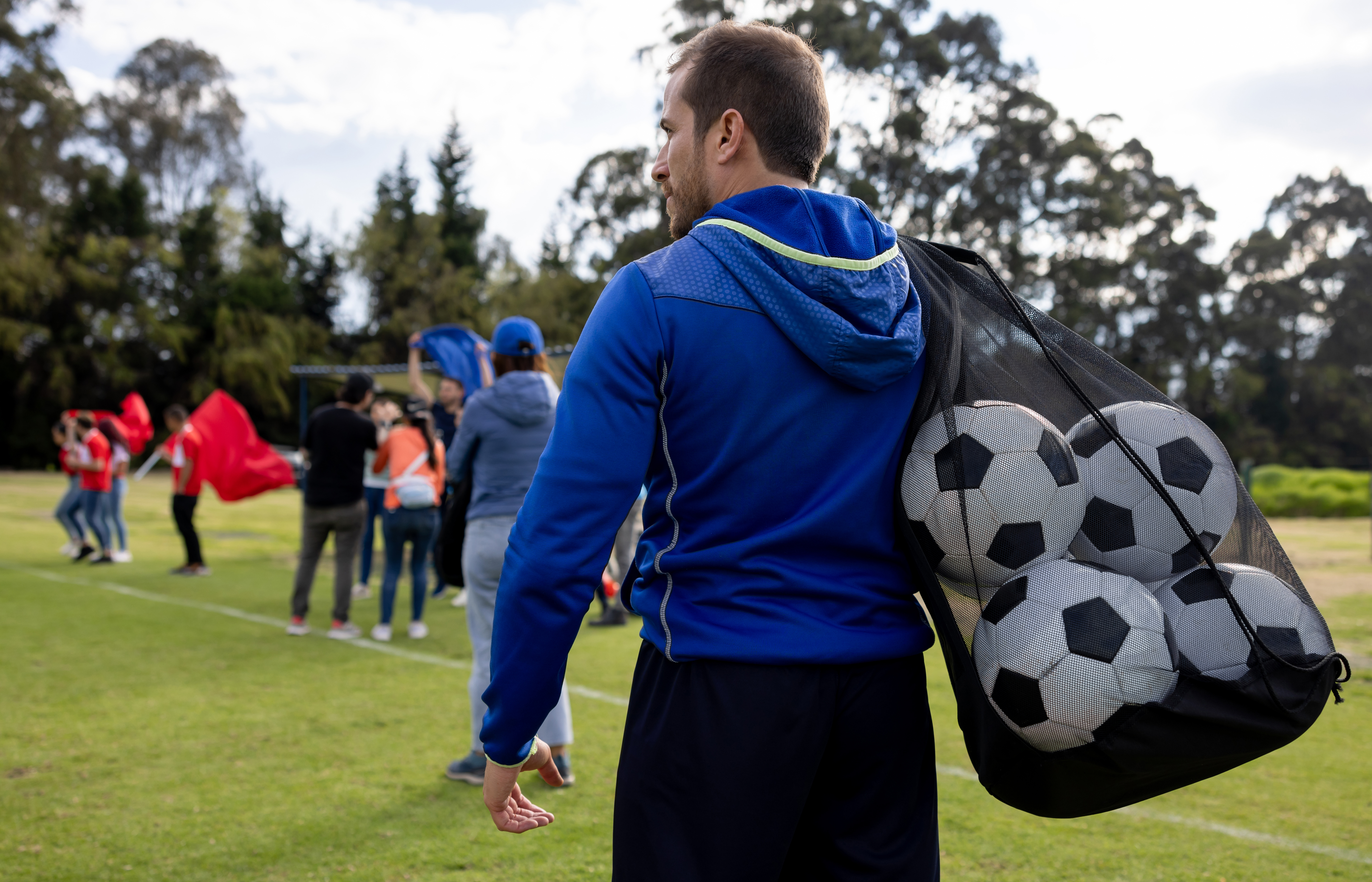 Coach met voetballen in net over de schouder