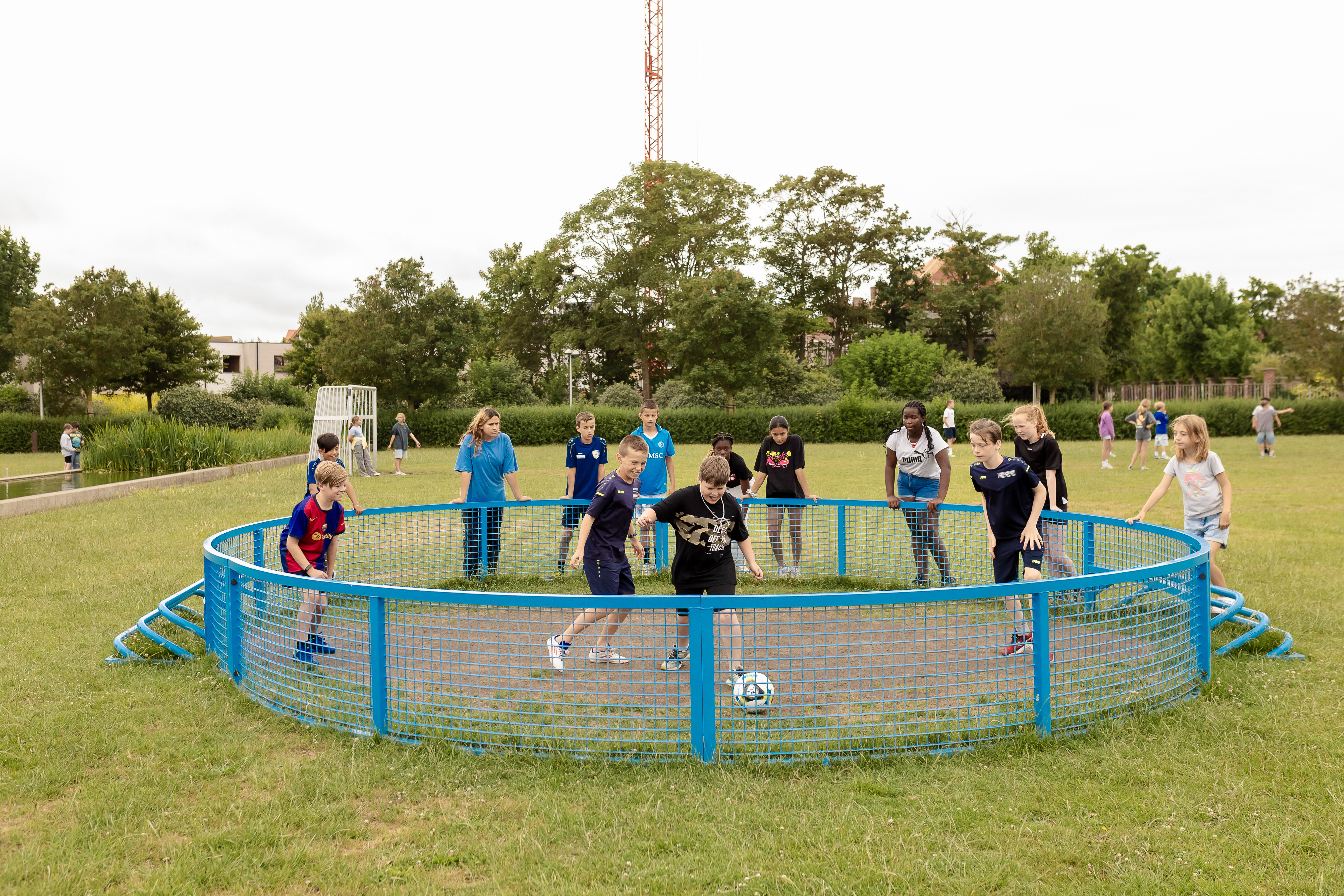 4 jongens spelen voetbal in pannakooi, jongeren supporteren rond pannakooi