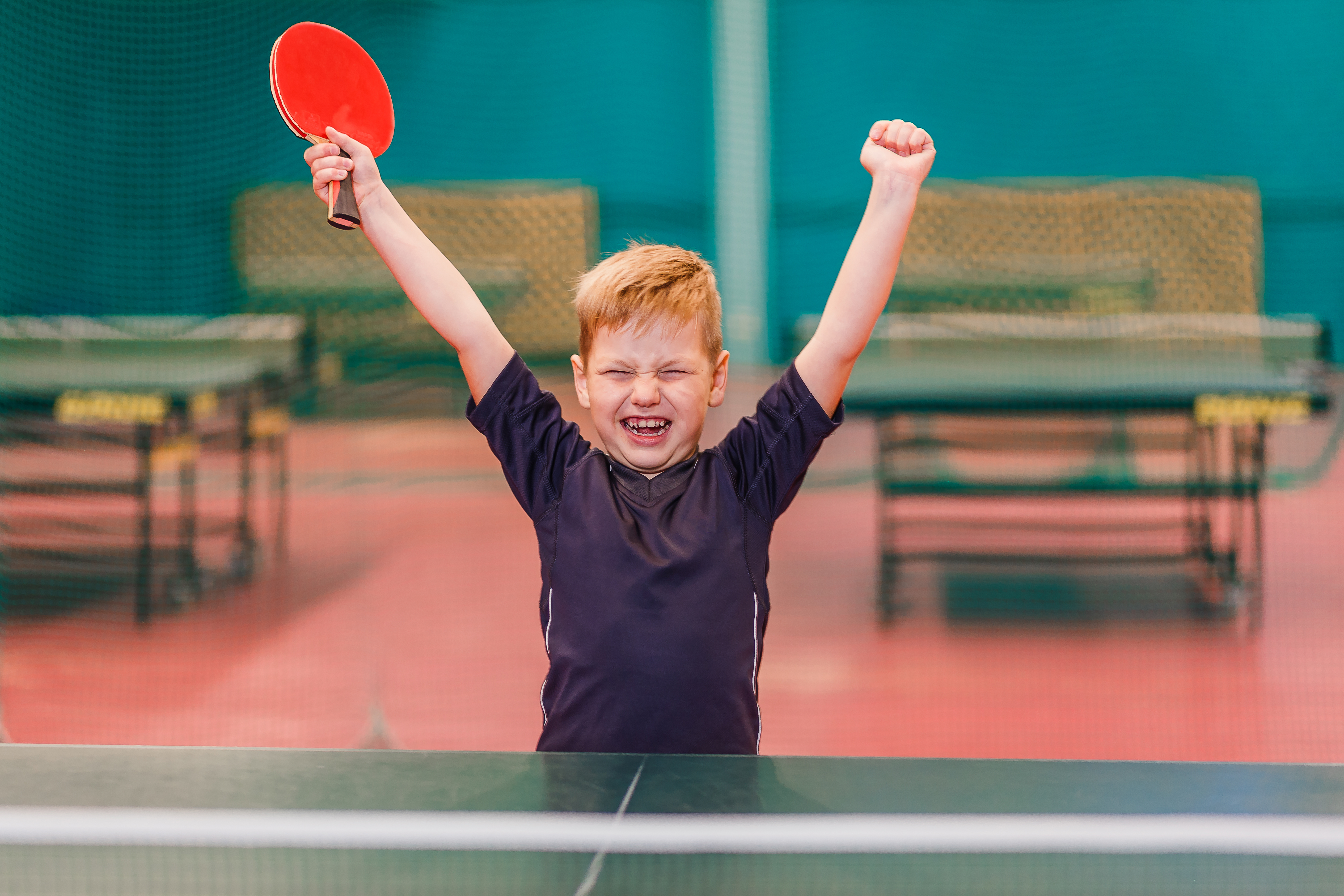Jongen wint bij tafeltennis en steekt handen in de lucht, en in een hand een pallet