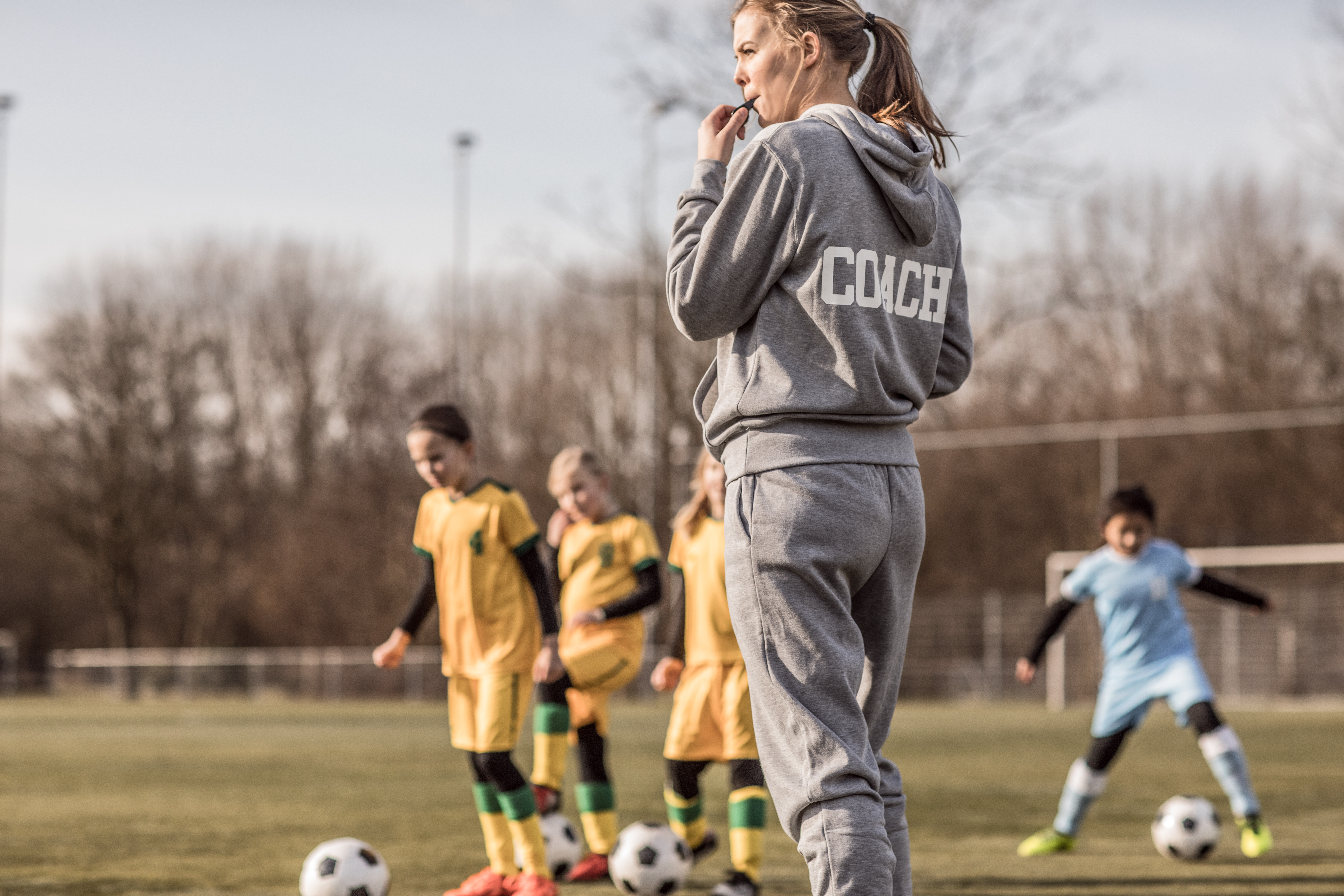 Jonge vrouwelijke voetbalcoach met haar meisjesteam blaast op fluitje