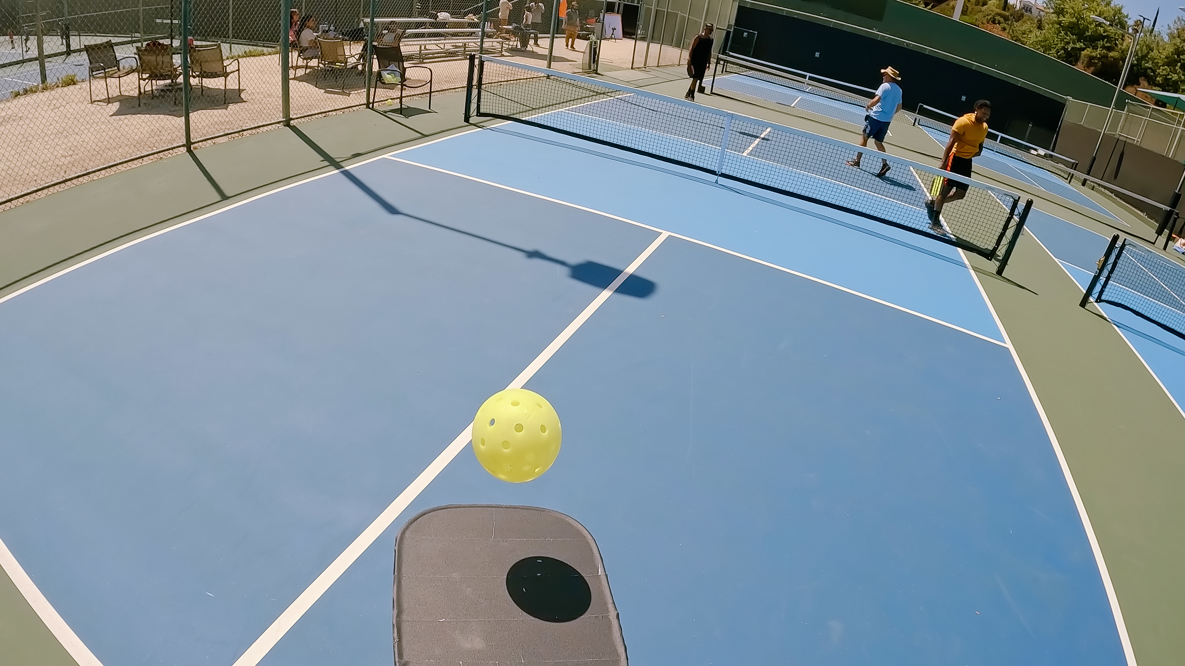 Personal point of view shot from the perspective of a pickleball player juggling a ball as other players get into position for a doubles game.