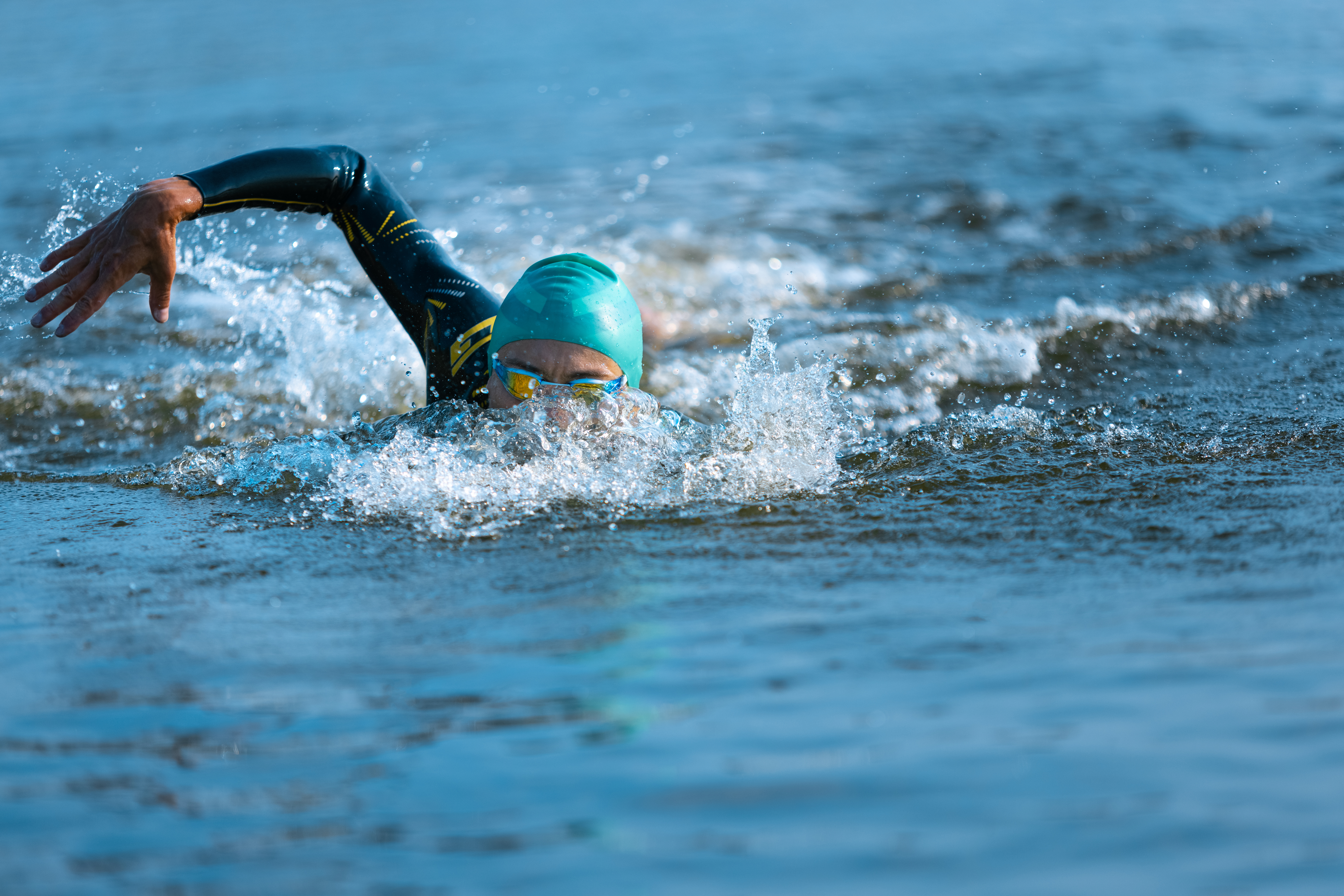 Professional triathlete swimming in river's open water. Man wearing swim equipment practicing triathlon on the beach in summer's day. Concept of healthy lifestyle, sport, action, motion and movement.